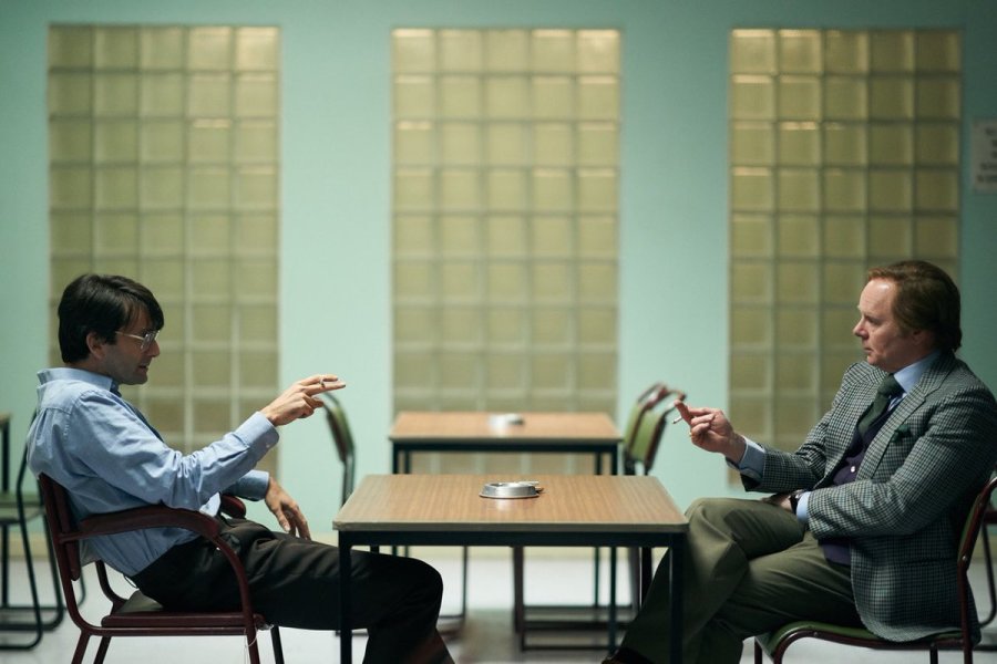 Dennis Nilse (David Tennant) i Brian Masters (Jason Watkins) siedzą naprzeciw siebie w więziennym pomieszczeniu przeznaczonym na spotkania. Obaj palą papierosy.